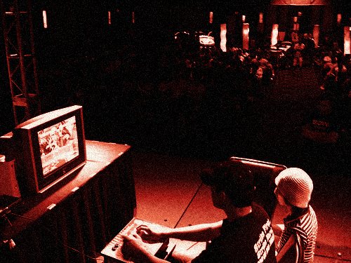 Alex at the stage machine in a Cobra Kai shirt, seen from behind, the crowd in front of him